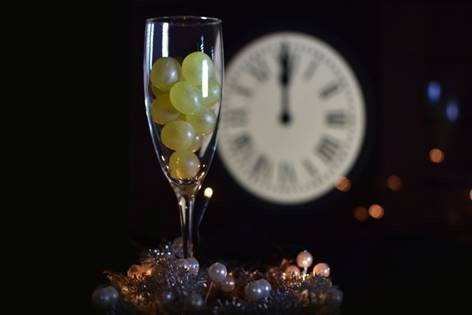 A champagne flute filled with grapes, with a clock striking 12 midnight in the background