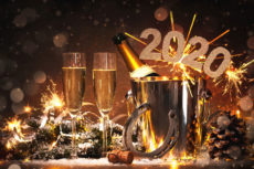 Two glasses of champagne and the bottle in an ice bucket, with 2020 numbers and sparklers