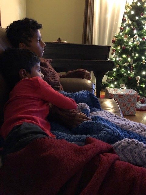 Two boys curling up on the couch to watch Christmas movies with their mom