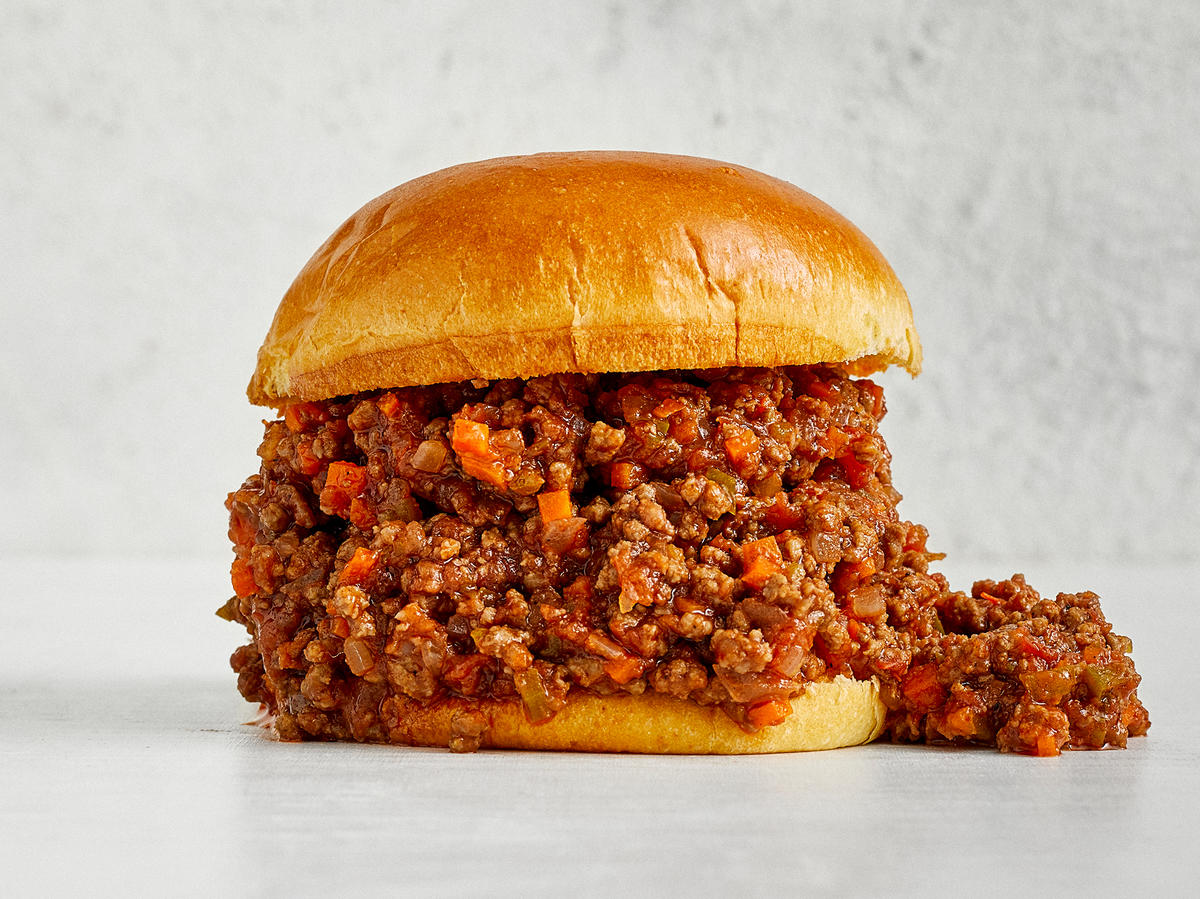 sloppy joe with meat and sauce mix on a hamburger bun on a grey counter with grey stucco wall behind
