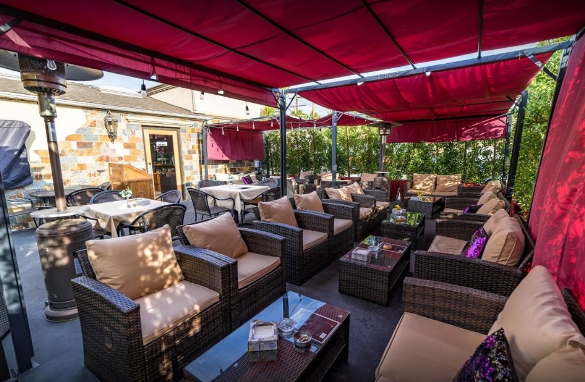 red awning back patio dining with lounge chairs and couches small coffee tables purple sequin pillows beige cushions brick wall heat lamps