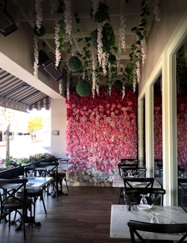 outdoor patio dining surrounded by flowers pink roses white hanging flowers white marble tables with black metal chairs and wood floor