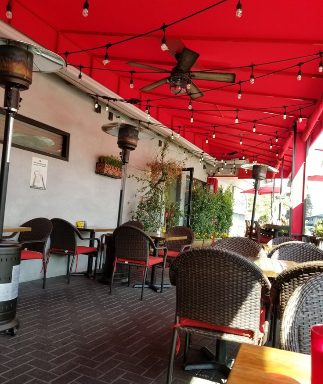 red maple cafe with red overhang strung with lights a brown ceiling fan heater lamps grey brick floor outdoor dining wicker brown chairs with red cushions plants 