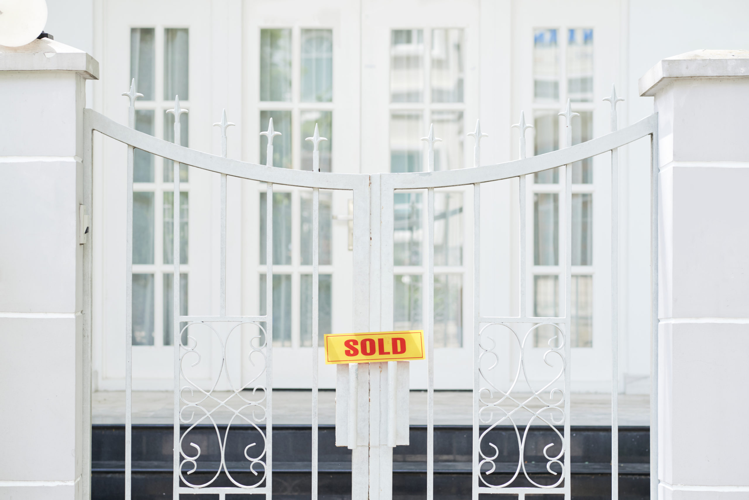 Sign that says "sold" on the gate of a large home