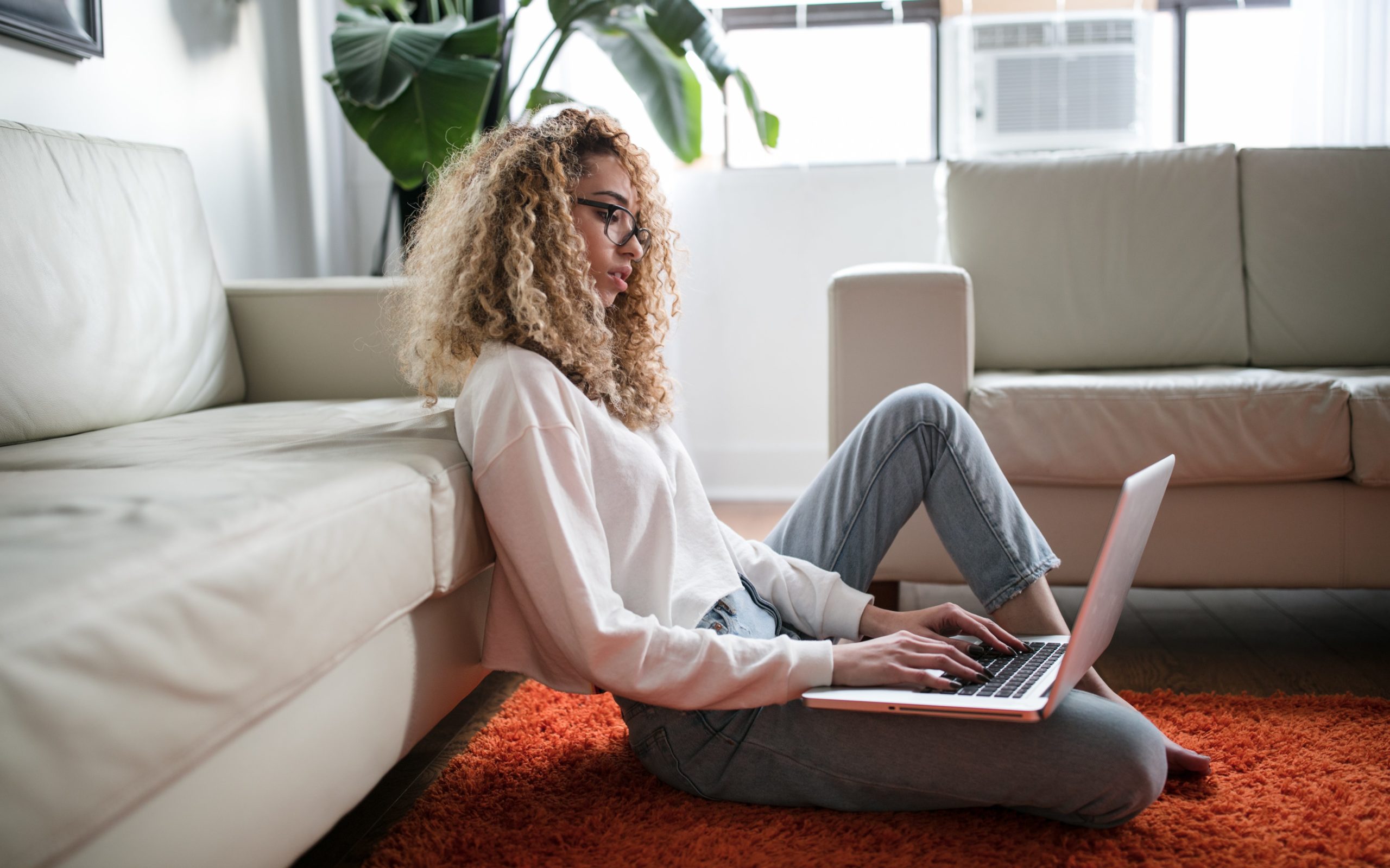 young woman is working on her laptop sitting on the floor of her living room