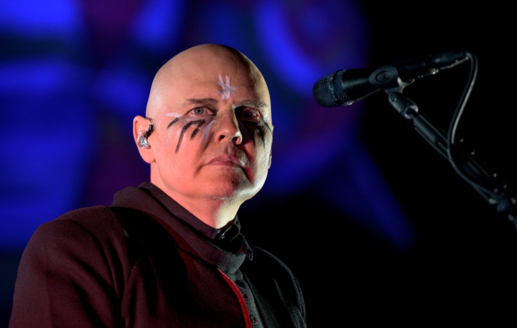 Smashing pumpkins performing live in concert with face paint and blue lighting. 
