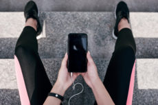 a woman holding a phone inbetween her legs while plugged into headphones