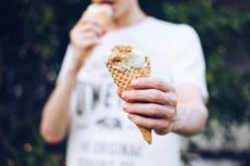 man eating ice cream melting down the cone while holding it in his hand
