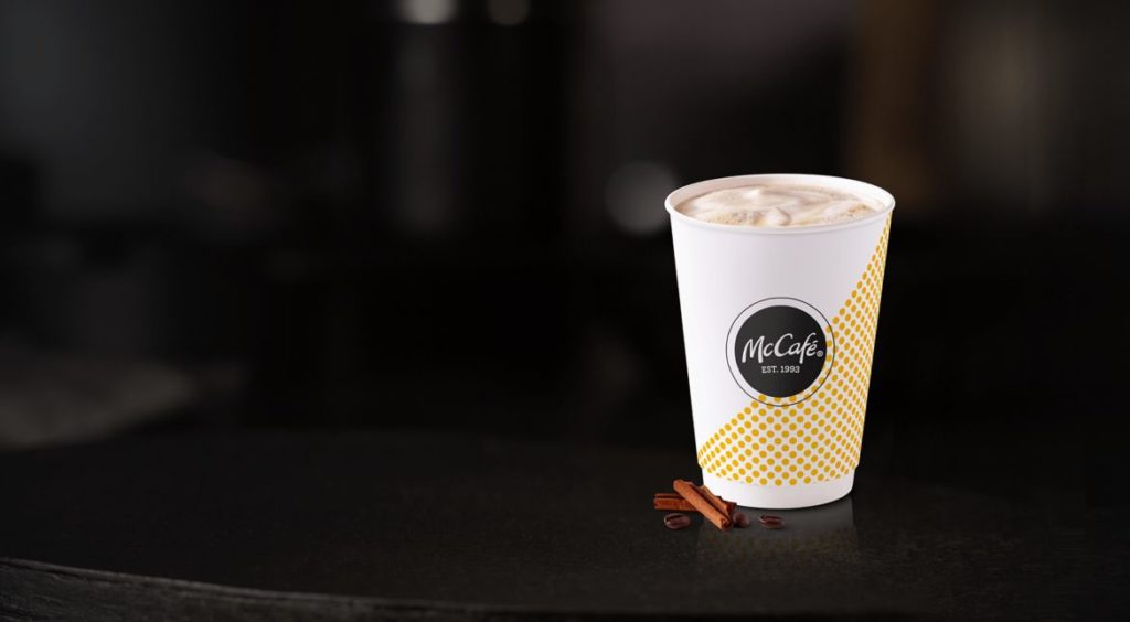 McDonald's pumpkin spiced latte in a McCafe cup with two cinnamon sticks in front of it on a black blurred background