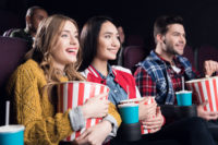 young smiling friends with popcorn watching film in movie theater watching movies coming out this september