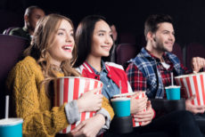 young smiling friends with popcorn watching film in movie theater watching movies coming out this september