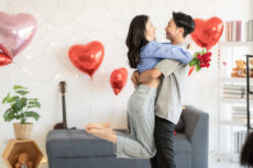 Asian couple holding each other with heart shaped balloons in the background