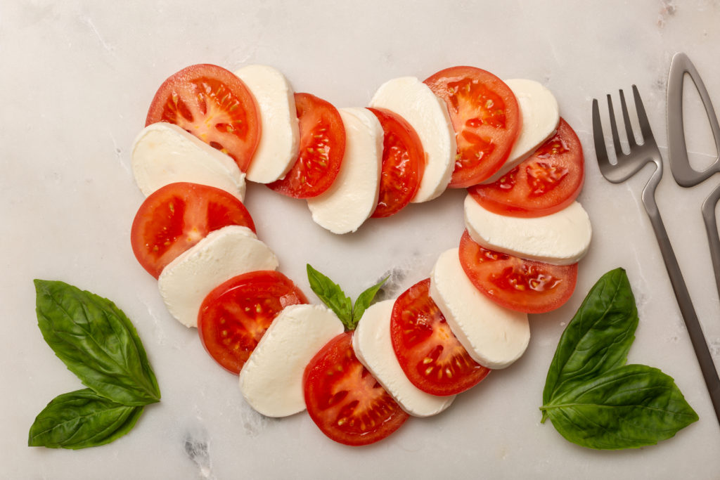 Caprese salad arranged in a heart shape with fork and knife for Valentine's Day.