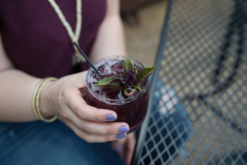 girl with purple nails holding blueberry margarita with basil.