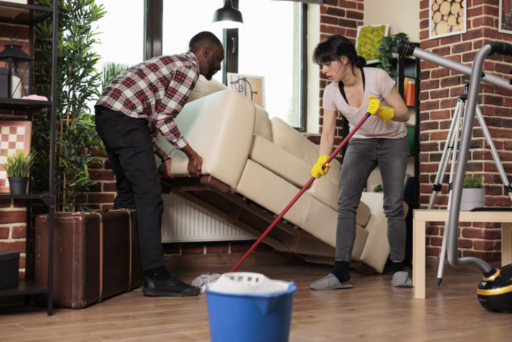 Interracial couple lifting furniture and mopping loft-style home.